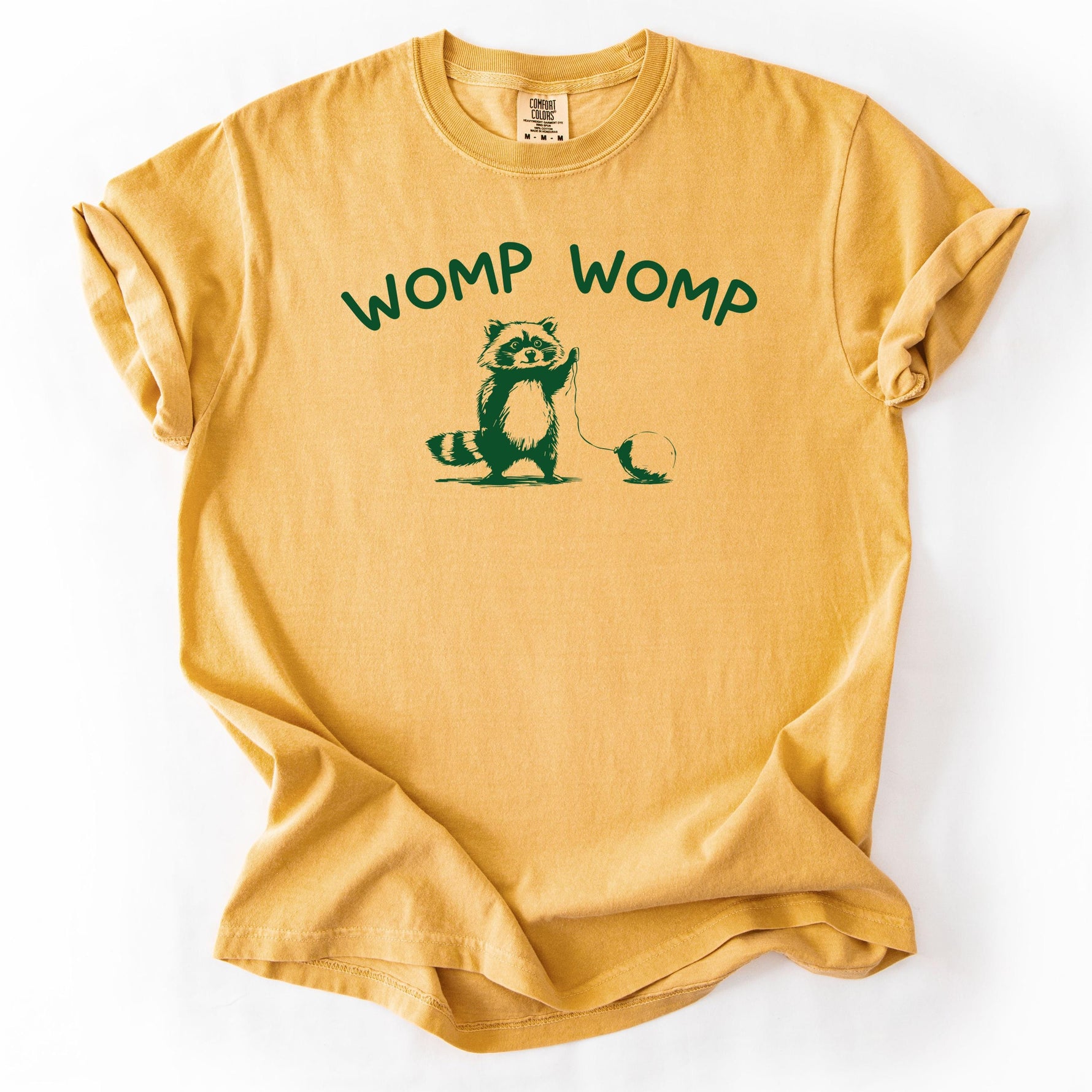 Mustard yellow t-shirt with raccoon graphic and WOMP WOMP text.